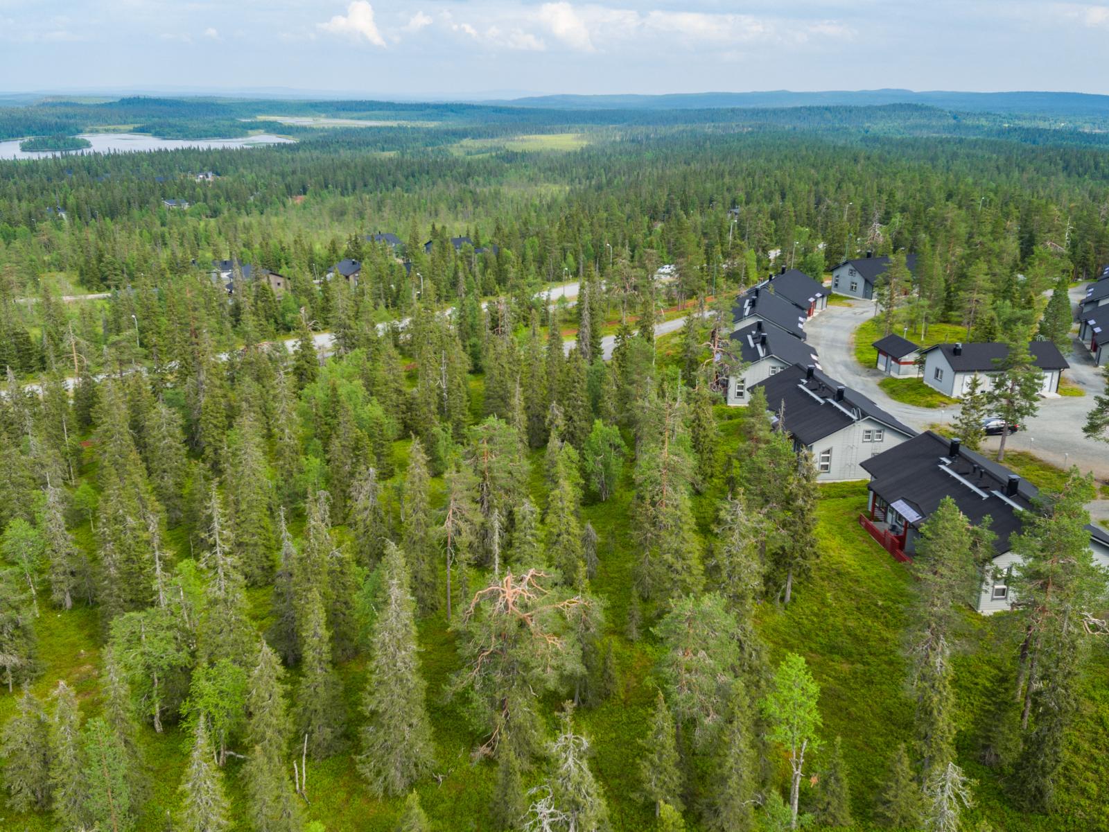 Matkailukeskuksen mökkialueella risteilee teitä. Taka-alalla on järvi ja vaaroja. Ilmakuva.