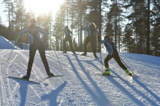 Neljä hiihtäjää nousee vauhdilla mäkeä ylös aurinkoisena talvipäivnä.