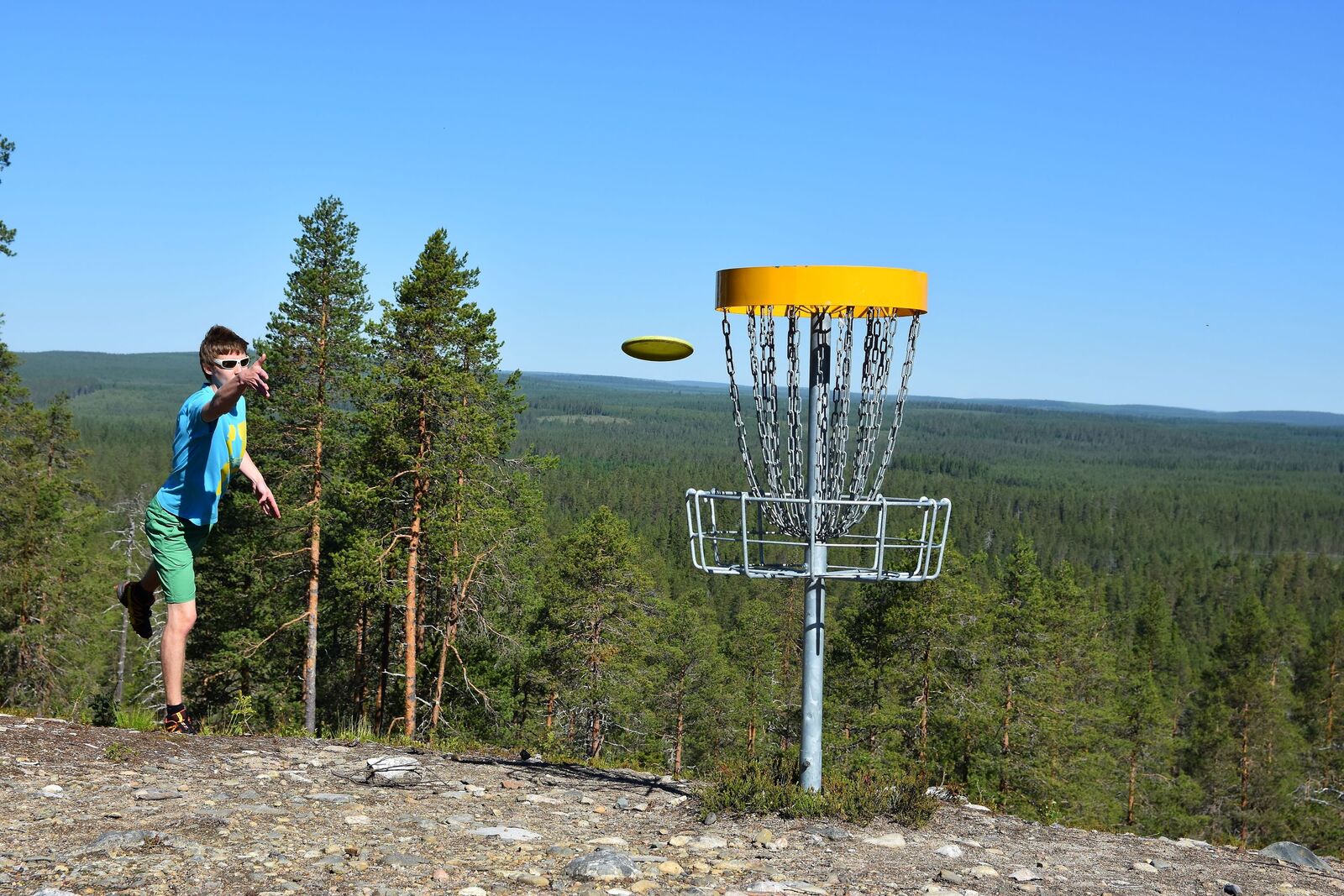 Henkilö heittää frisbeegolf-kiekkoa maaliin kesäisessä tunturimaisemassa.