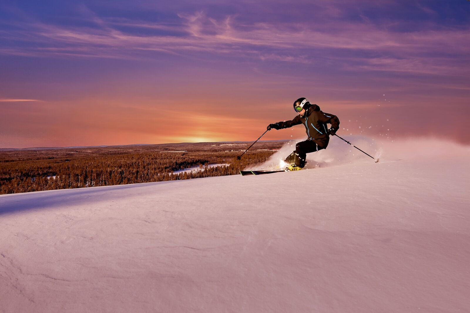 Laskettelija laskemassa auringonlaskun aikaan tunturin päältä.