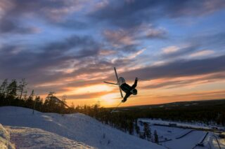 Freestylelaskija tekee ilmavan tempun auringonlaskun aikaan rinteessä.