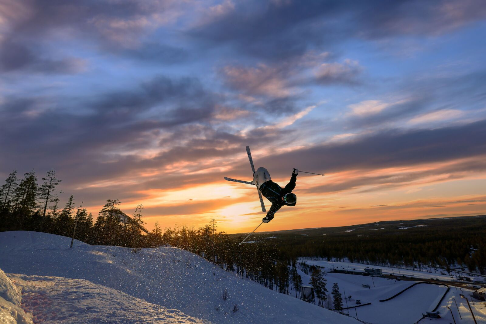 Freestylelaskija tekee ilmavan tempun auringonlaskun aikaan rinteessä.