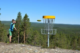 Pelaaja heittää frisbeegolf-kiekkoa kohti pesää vaaran laella.