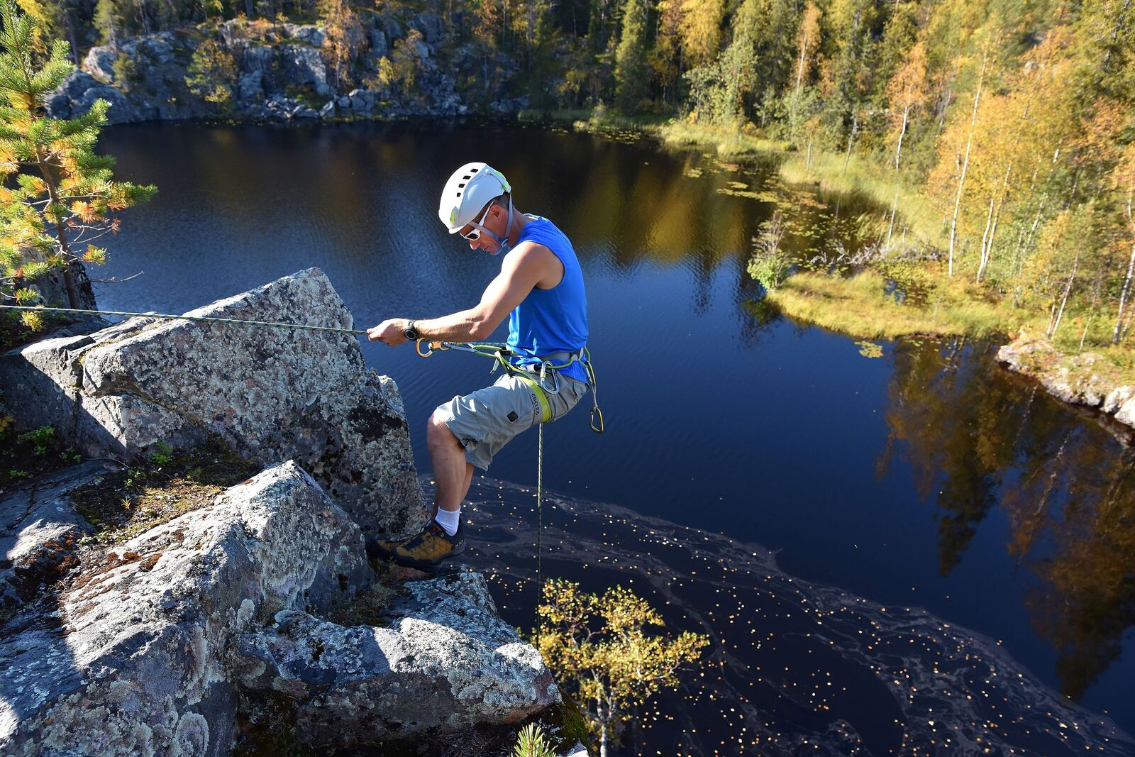 Kalliokiipeilijä on laskutumassa kohti alhaalla näkyvän lammen rantaa.