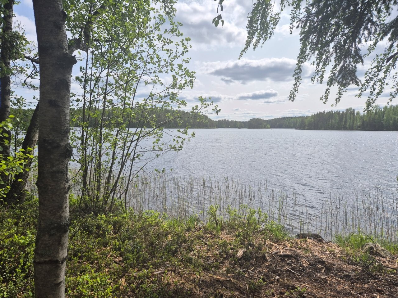 Maisema järvelle, taivaalla on pilviä, aurinko paistaa.