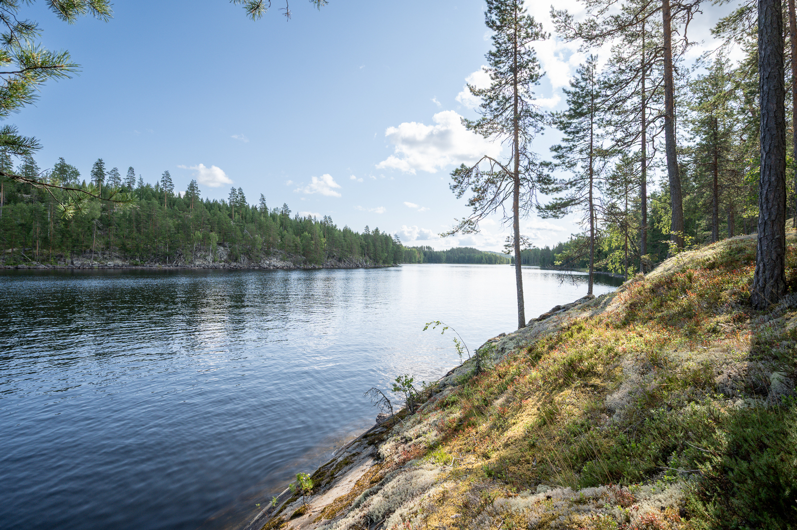 Rantakalliolle paistaa aurinko, vastarannalla näkyy kalliota ja metsää.