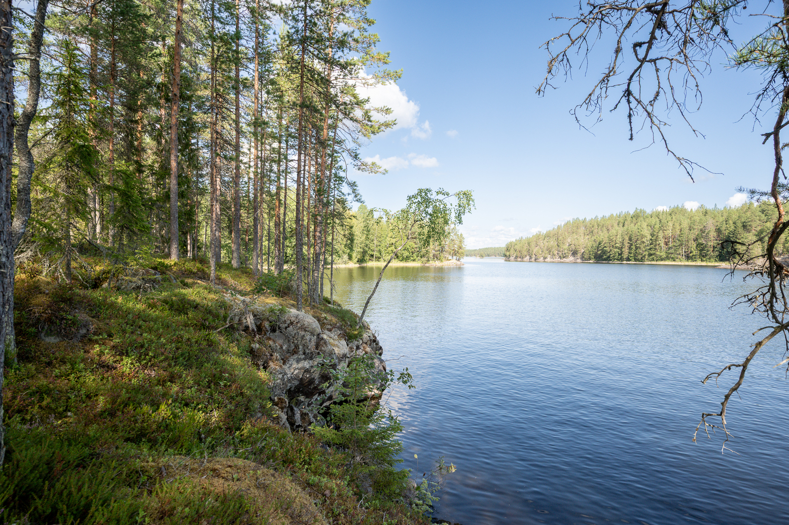 Varjoisa rantakallio, aurinko paistaa vastarannalle.