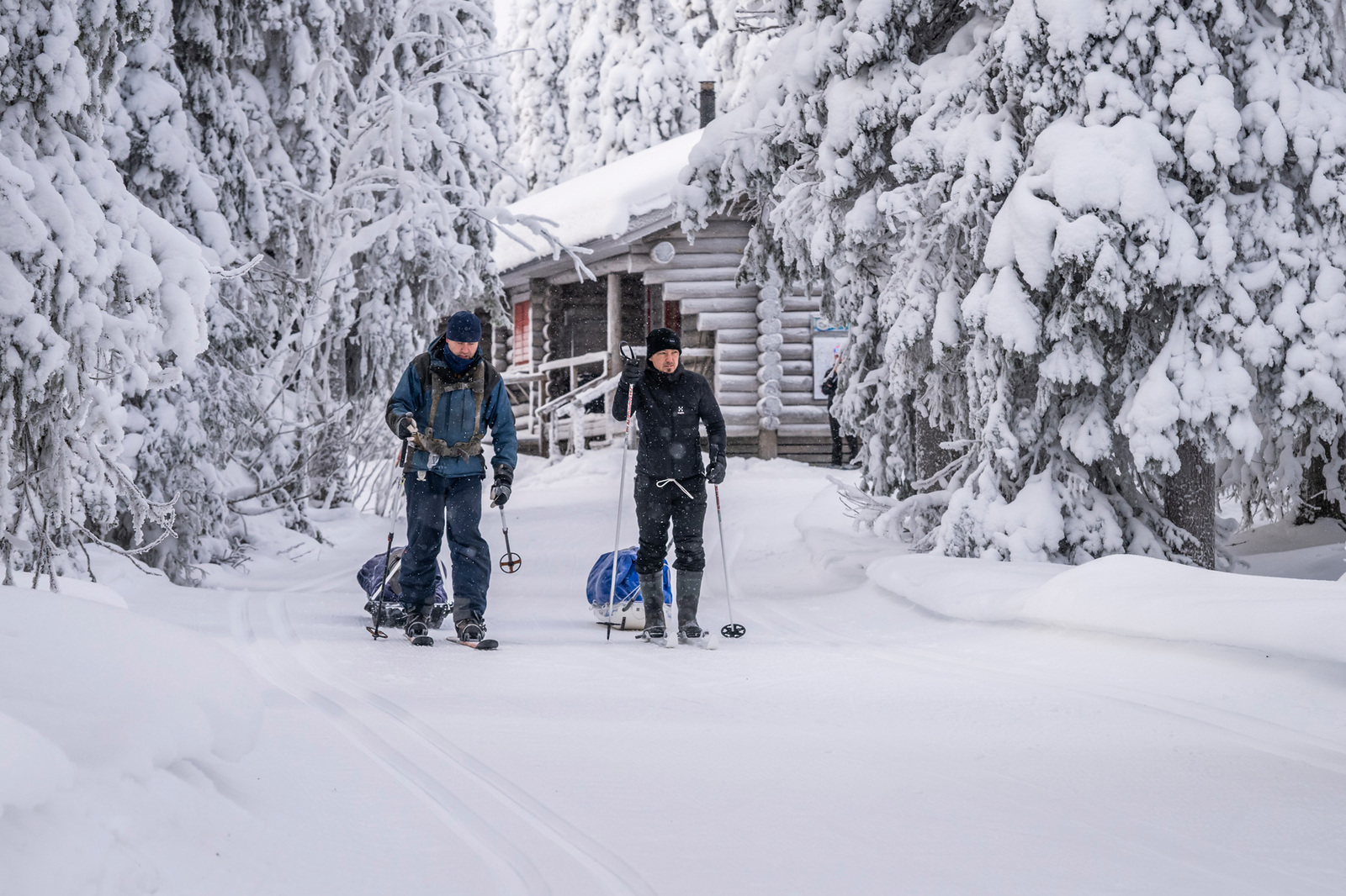 Kaksi henkilö hiihtävät liukulumikengillä ja vetävät ahkioita perässään.