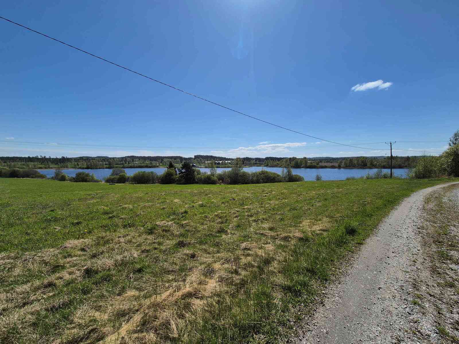 Maalaismaisemassa kulkeva hiekkatie, kaukaisuudessa näkyy järvi, etualalla on peltoa.