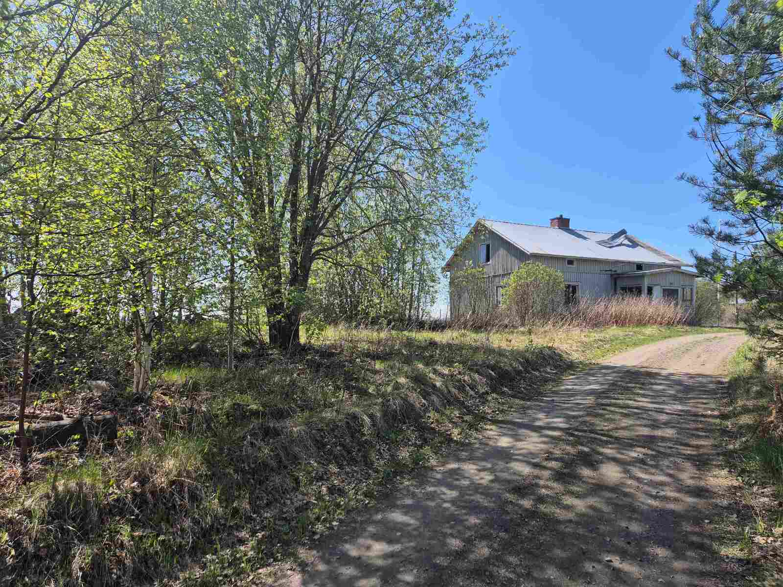 Hiekkatie johtaa vanhalle ränsistyneelle talolle, aurinko paistaa ja taivas on pilvetön.