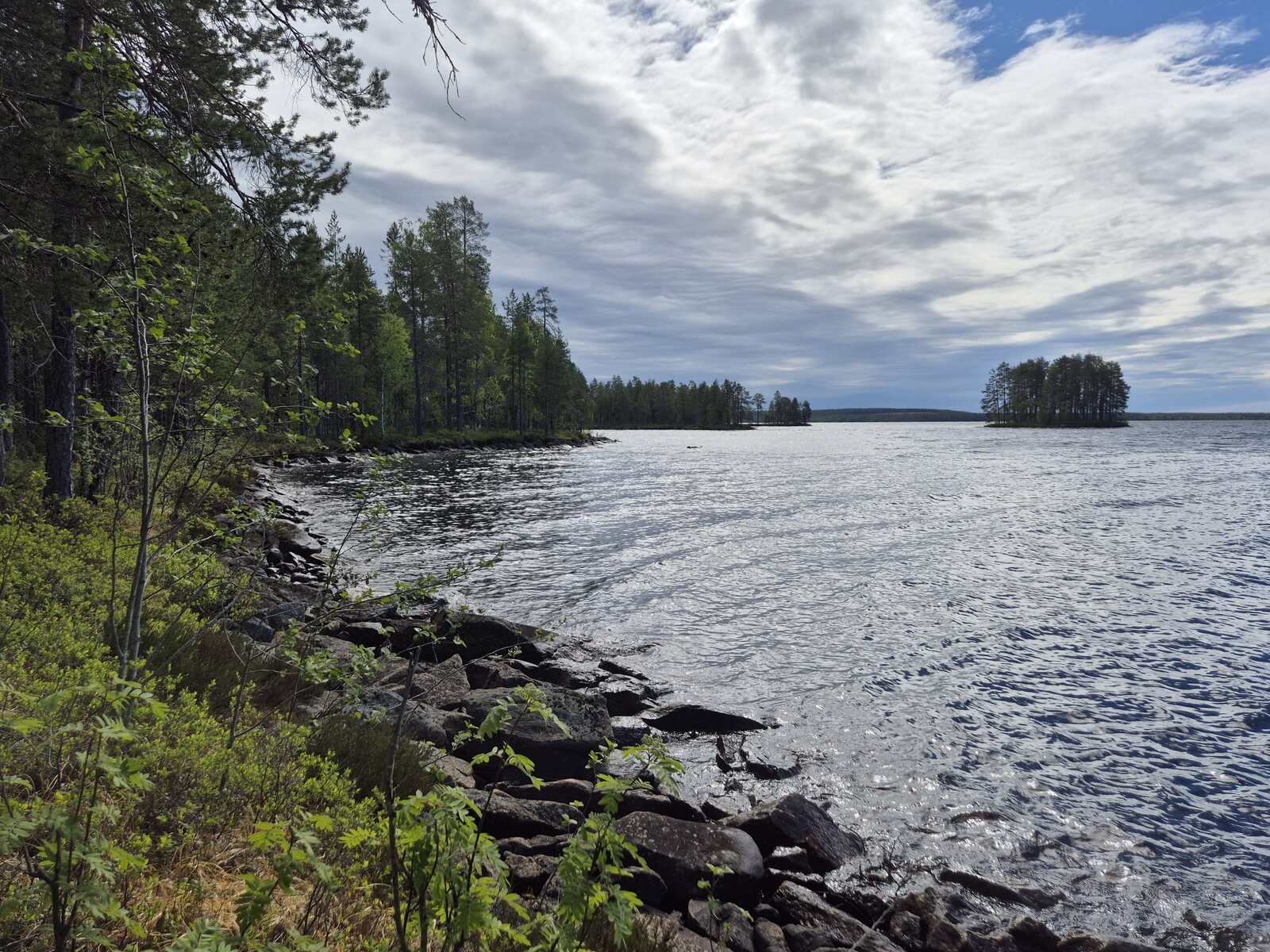 Tontin ranta on kivikkoinen, kauempana näkyy saari.