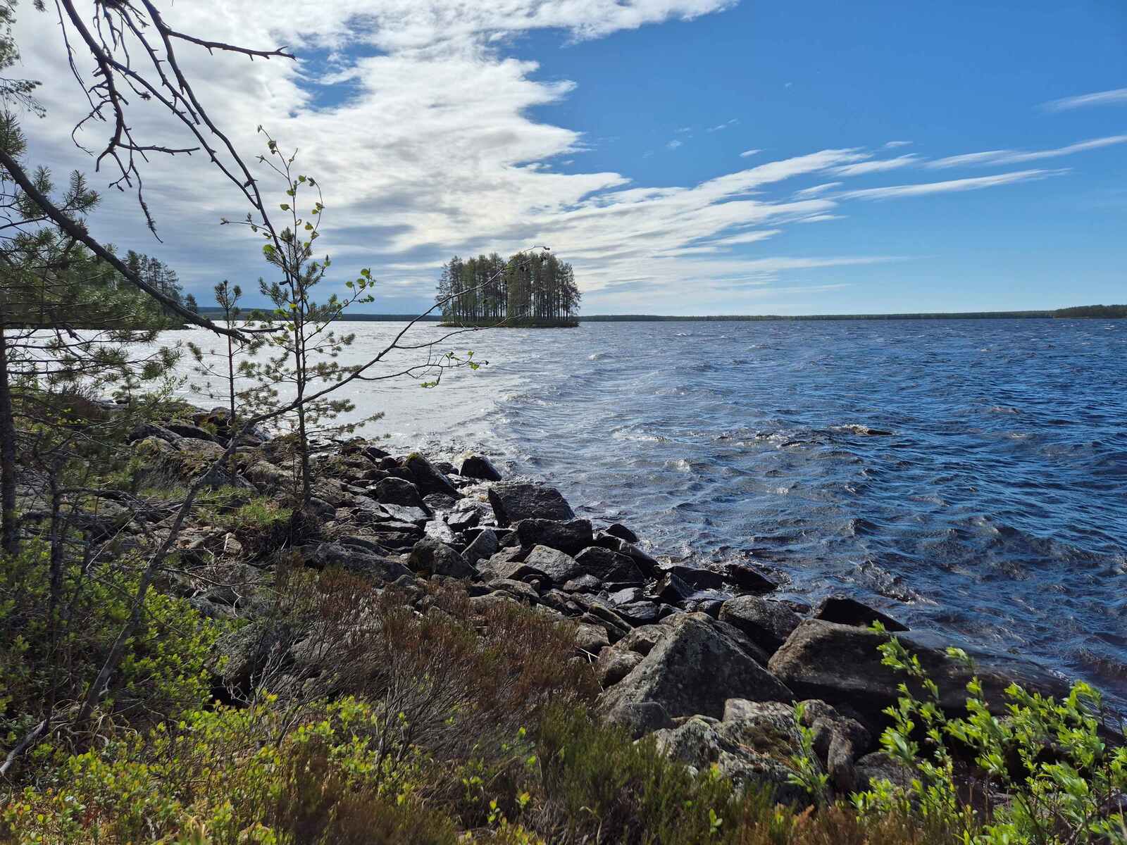Tontin kivikkoinen ranta, kauempana järvellä näkyy saari.