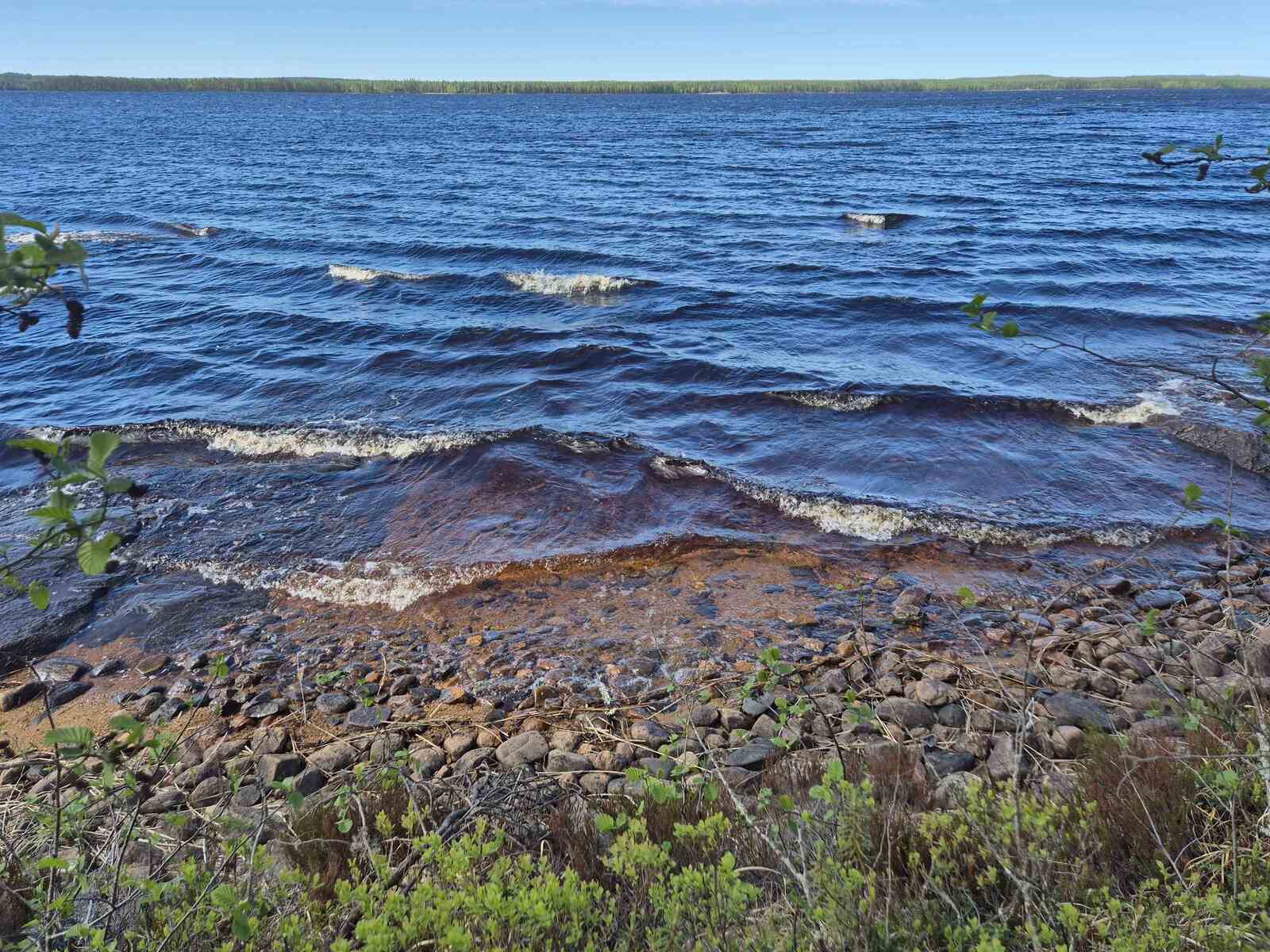 Aallot lyövät tontin rantaan vaahtopäisinä, ranta on pientä kiveä ja hiekkaa.