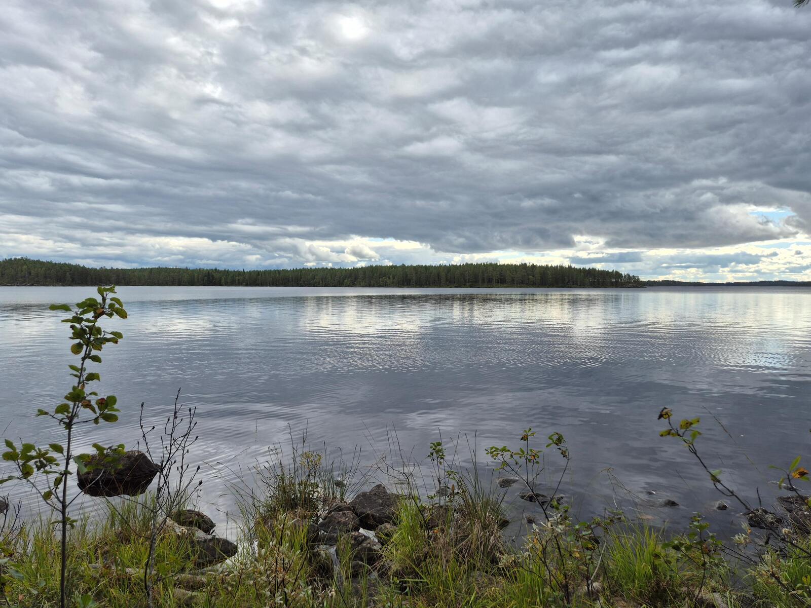 Järvimaisema, taivas on pilvinen, vesirajassa on paljon kiviä.