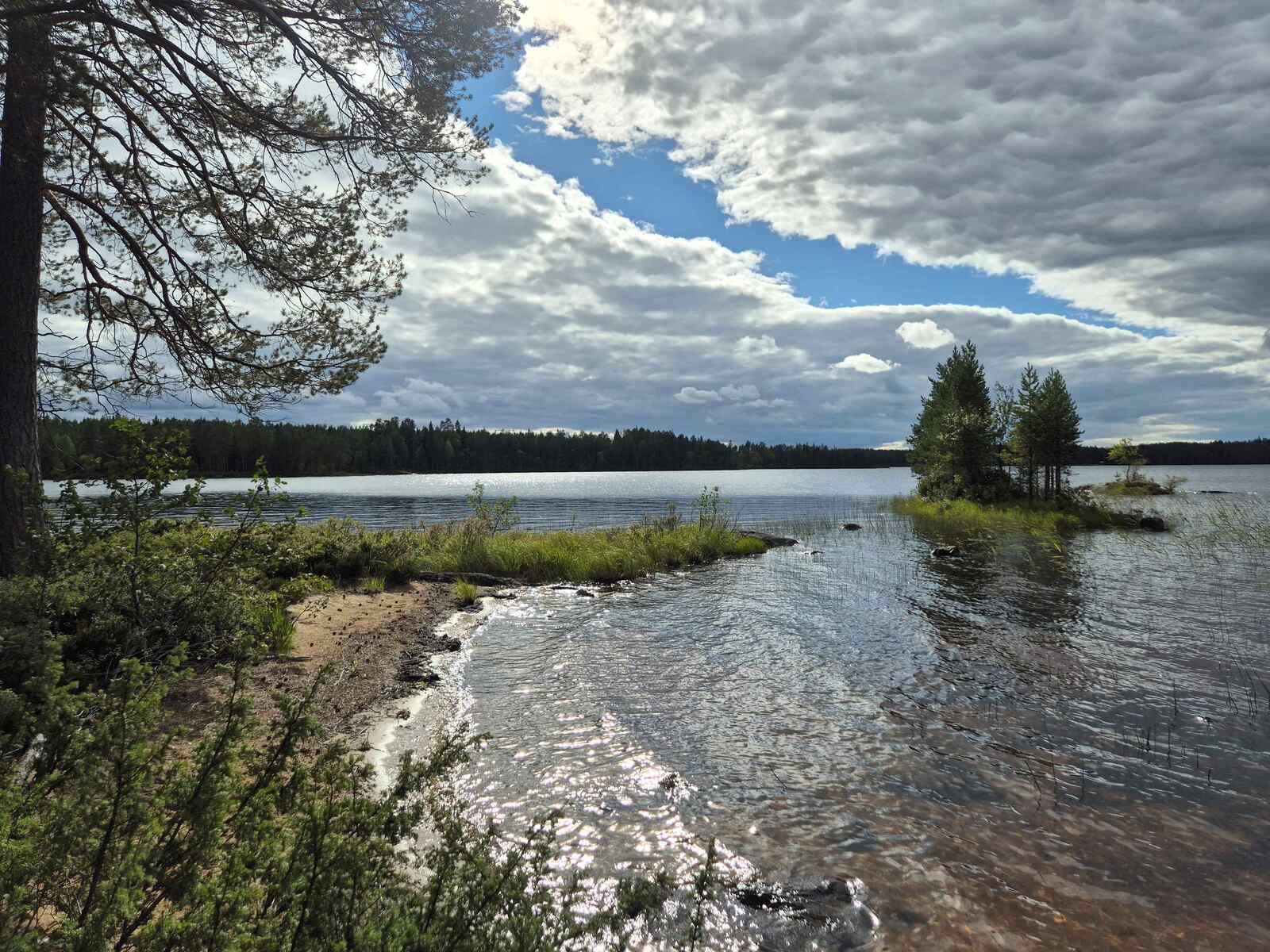 Maisema järvelle, luonnonhiekkarantaan lyö aallot, rannan läheisyydessä on pieni saari.