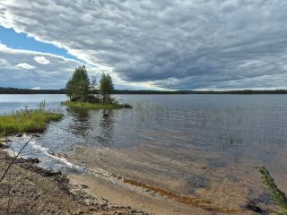 Maisema järvelle, luonnonhiekkarantaan lyö aalto, rannan läheisyydessä on pieni saari.