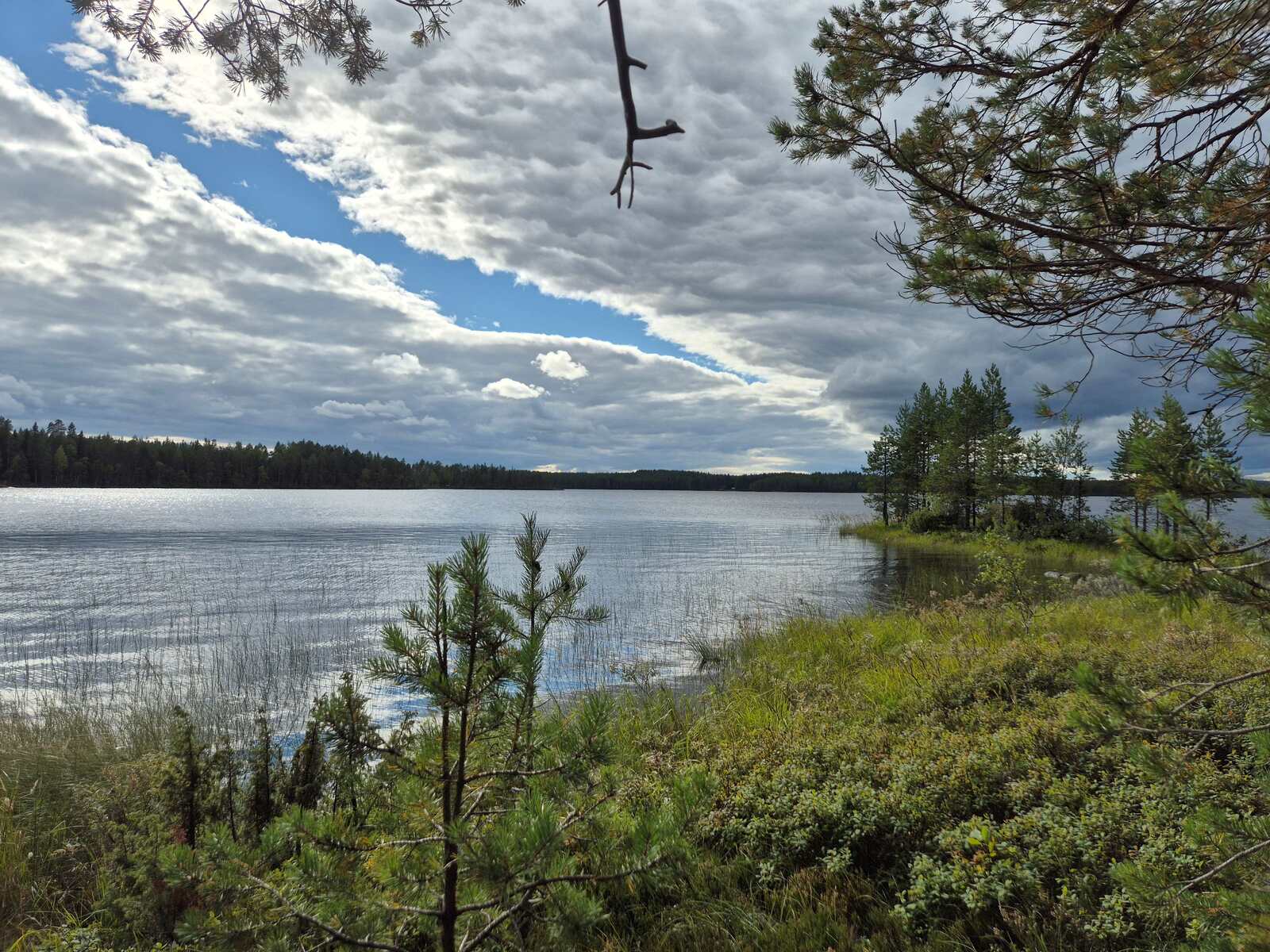 Järvimaisemassa on rannan edustalla pieni saari, taivaan pilviverhossa on yksi repeämä.